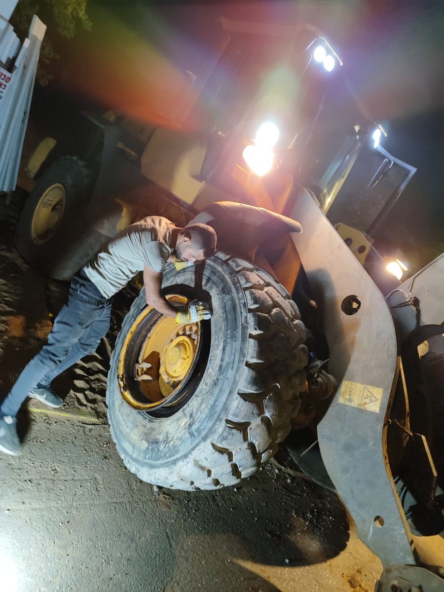 הטכנאי מרכיב צמיג של שופל בלילה, בתאורת הכלי, כדי שיחזור לעבודה כבר בבוקר.