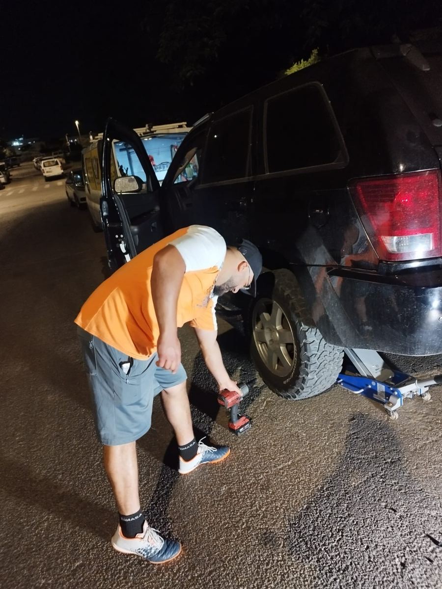 הטכנאי מחליף גלגל לג'יפ בלילה, עם ג'ק מקצועי ומברגת אימפקט.