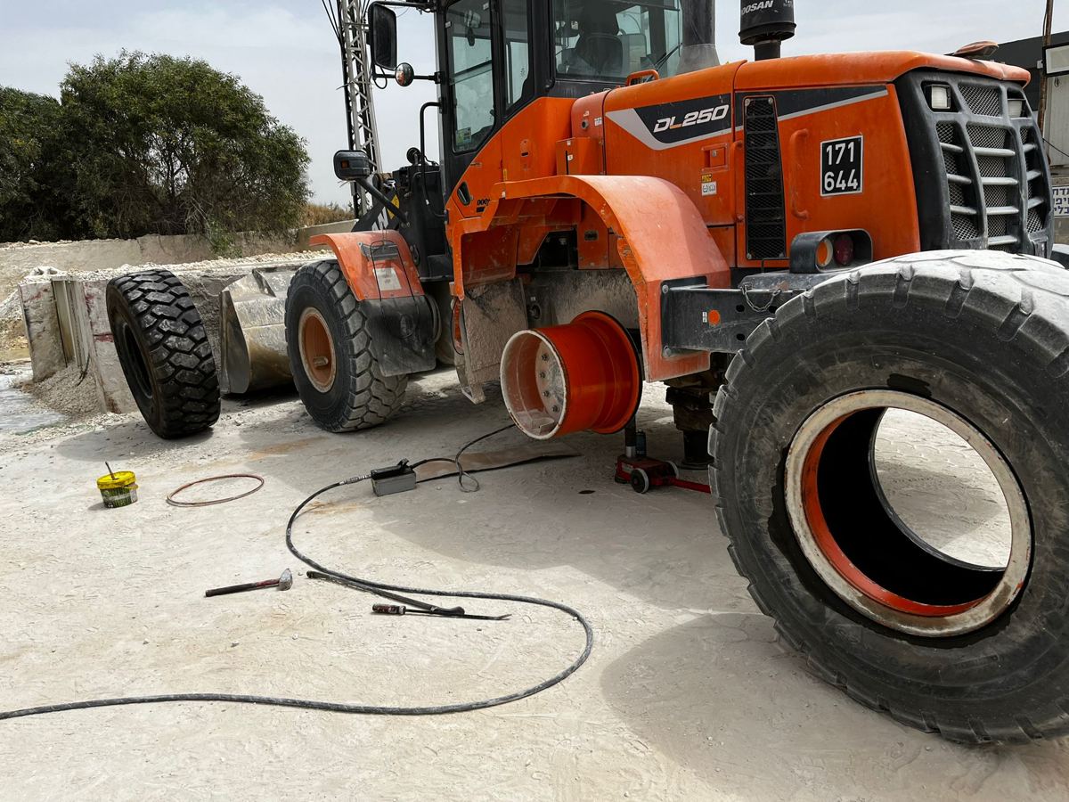 פירוק גלגל של שופל Doosan DL250 באתר העבודה. הרכב מורם על ג'ק הידראולי ותומכות, הצמיג הישן לימין והחדש מחכה להרכבה.
