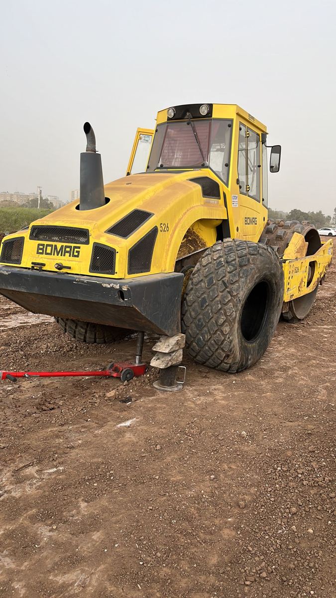 מכבש BOMAG מורם על ג'ק ותומכת בטיחות בשטח עפר, לפני החלפת הצמיג. לא צריך להוביל את הכלי לפנצ'ריה.