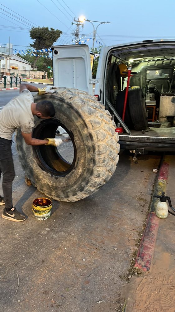 הטכנאי מרכיב צמיג גדול של כלי צמ"ה ליד רכב השירות