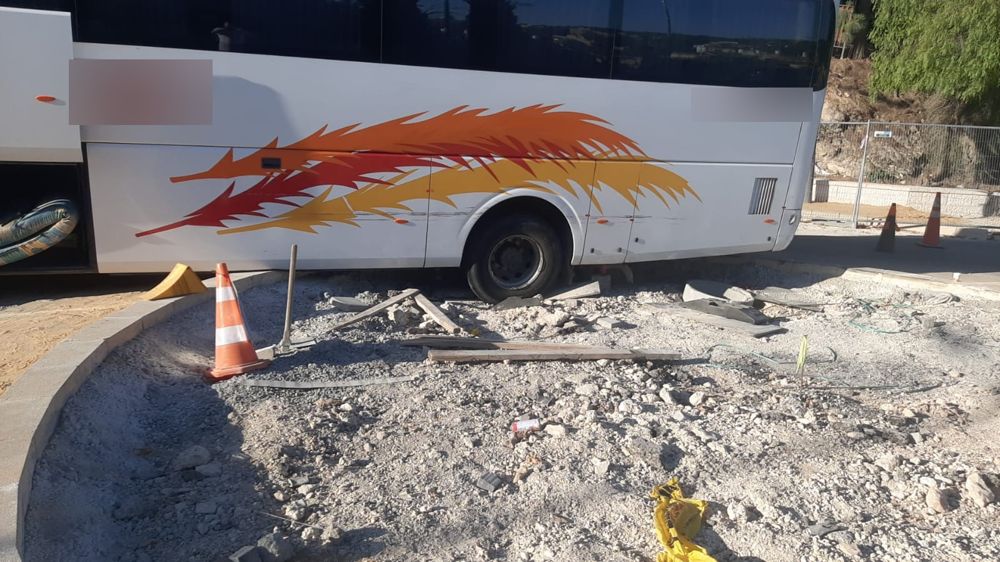 אוטובוס לבן שעלה על כיכר בבנייה בירושלים, הגלגל האחורי על אבנים ושברי אספלט, קונוסים וקרשים מסביב