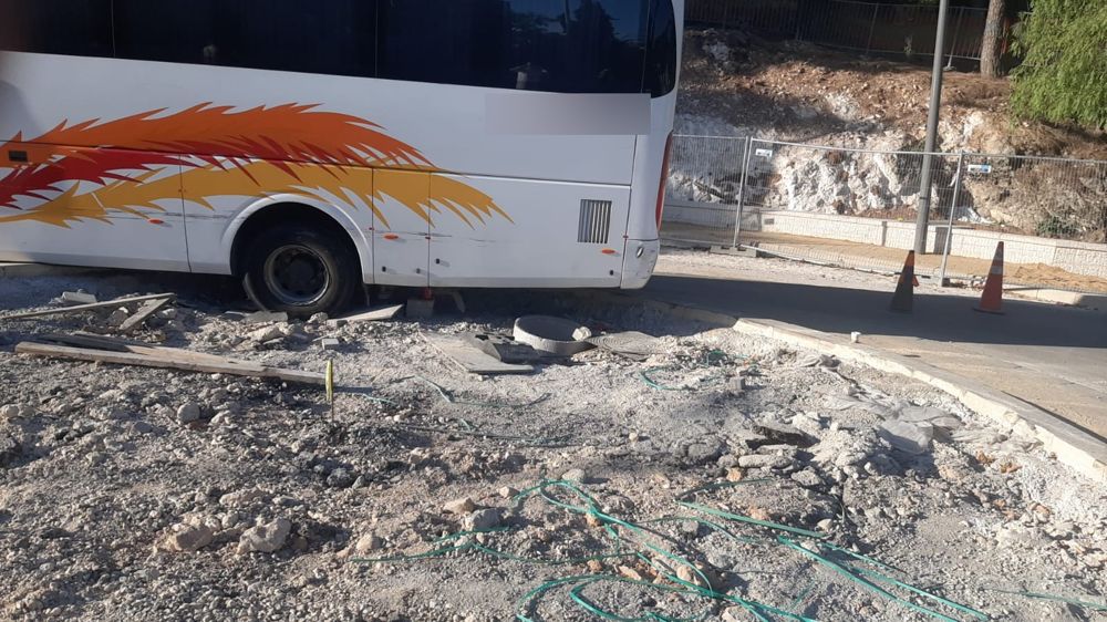 אוטובוס בכיכר בבנייה, הגלגל האחורי בין שברי אבן וקרשים, קונוסים מאחור