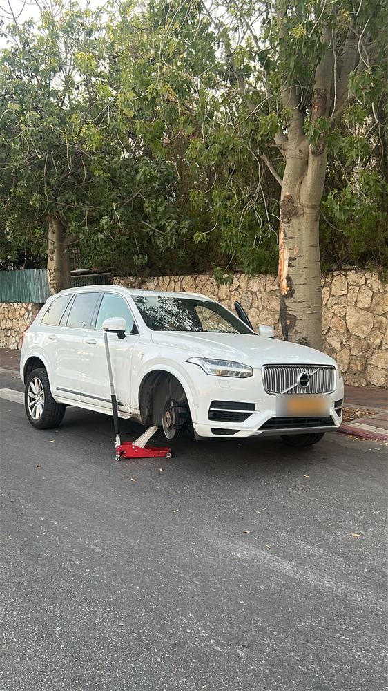 רכב שטח לבן מורם על ג'ק ברחוב שקט בירושלים, הגלגל הקדמי מפורק לפני החלפת צמיג