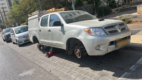 טנדר טויוטה מורם על ג'ק ליד בניין, שני הגלגלים בצד אחד מפורקים לפני הרכבת צמיגים חדשים