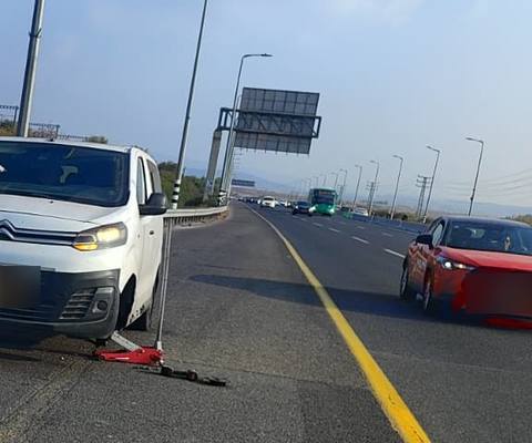רכב מסחרי לבן מורם על ג'ק בשול כביש מהיר, מכוניות חולפות בנתיב